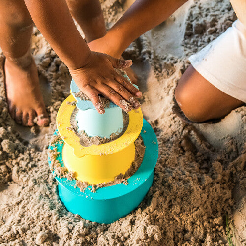 Kinderhanden vullen de gestapelde Quut zandstapeltoren alto met zand.