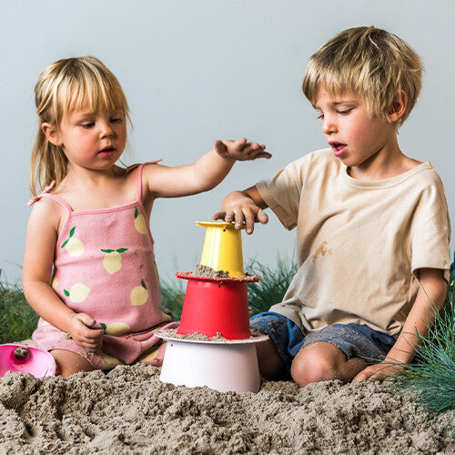 Twee kinderen stapelen de roze, rode en gele quut zandstapeltoren onderdelen op elkaar in het zand.