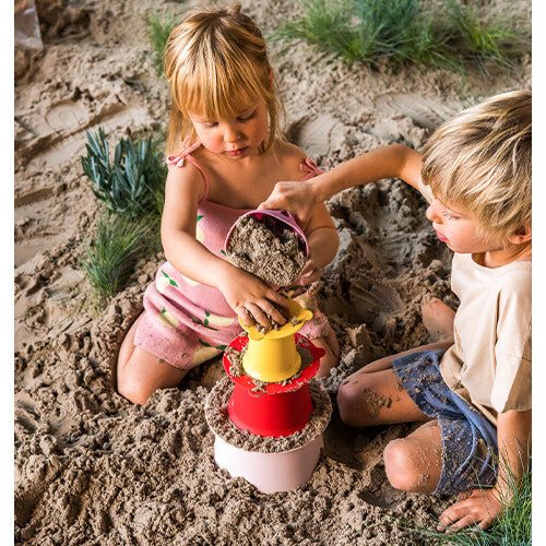 Twee kinderen vullen de quut zandstapeltoren onderdelen met zand om een zandkasteel te bouwen.