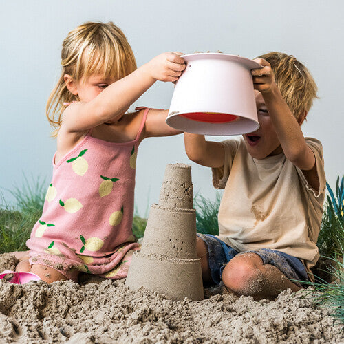 Twee kinderen spelen in het zand met een roze quut zandstapeltoren onderdeel en een zandkasteel.