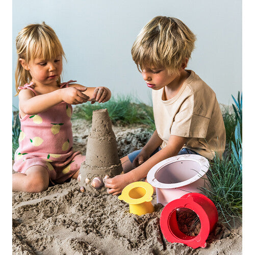 Twee kinderen spelen in het zand naast een zandkasteel en de losse quut zandstapeltoren onderdelen.