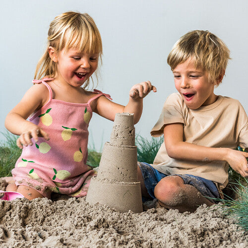 Twee lachende kinderen spelen in het zand naast een zandkasteel gemaakt met de quut zandstapeltoren.