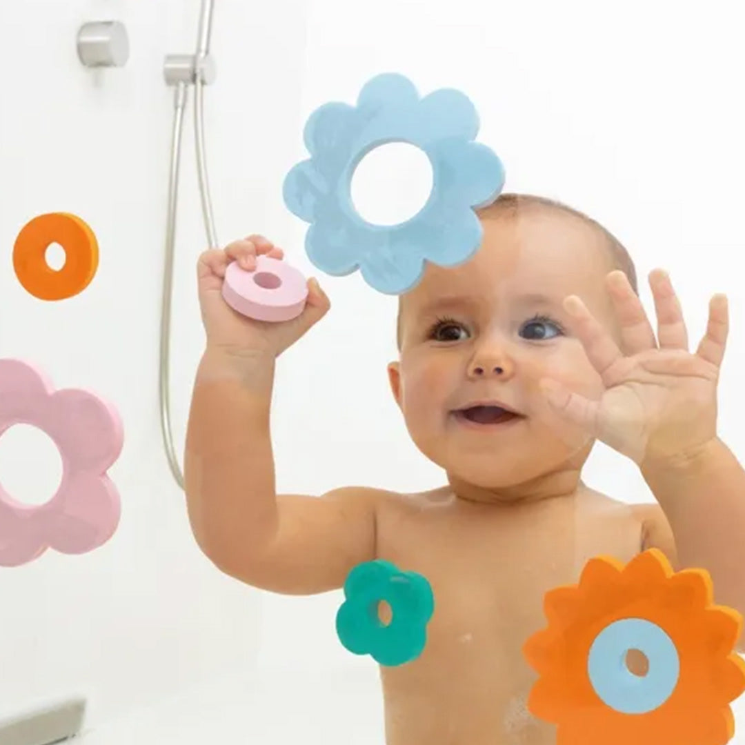 Een baby in de douche kijkt door een blauwe Quut badpuzzel bloemvorm.
