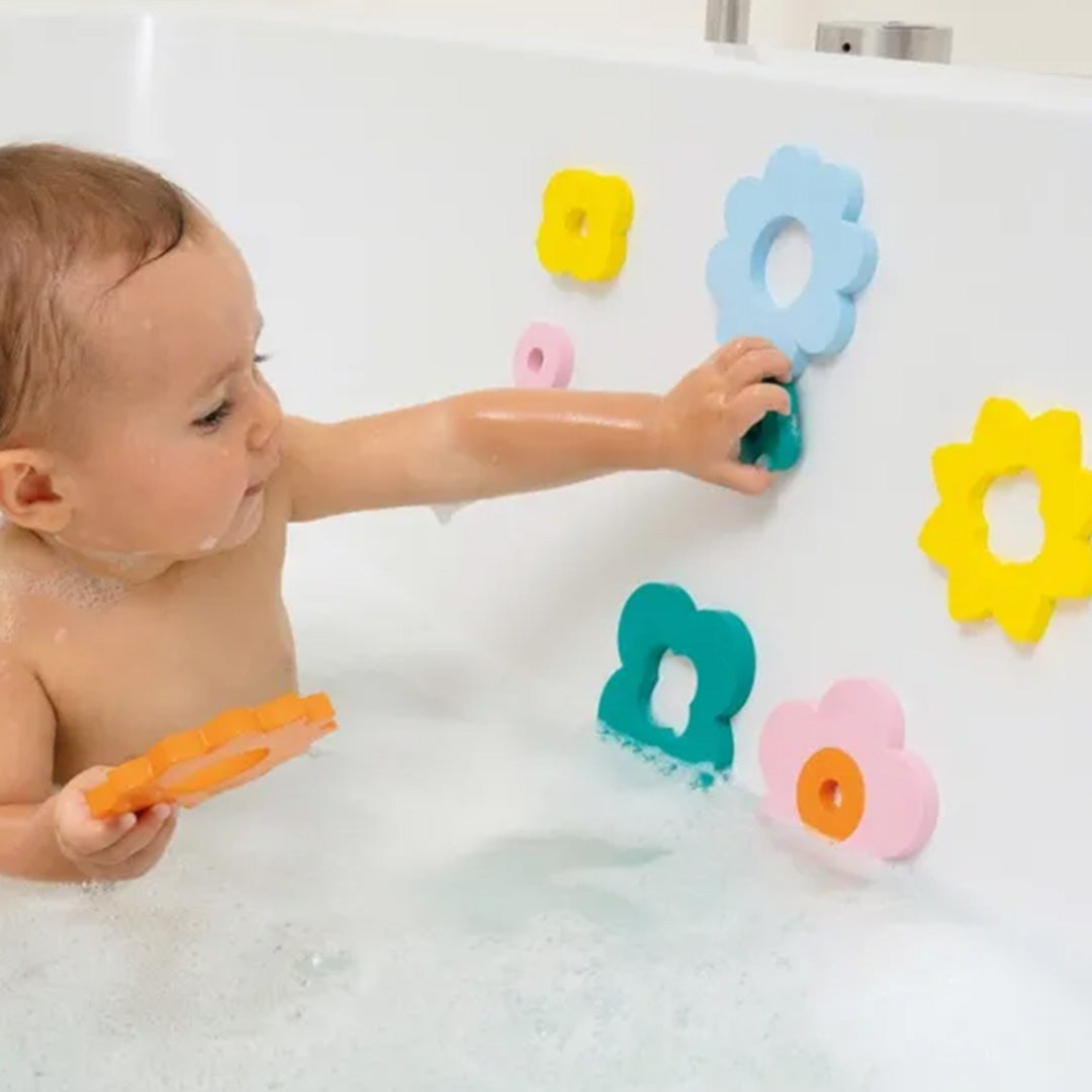 Een baby speelt in bad met de Quut badpuzzel bloemen die aan de tegelwand plakken.
