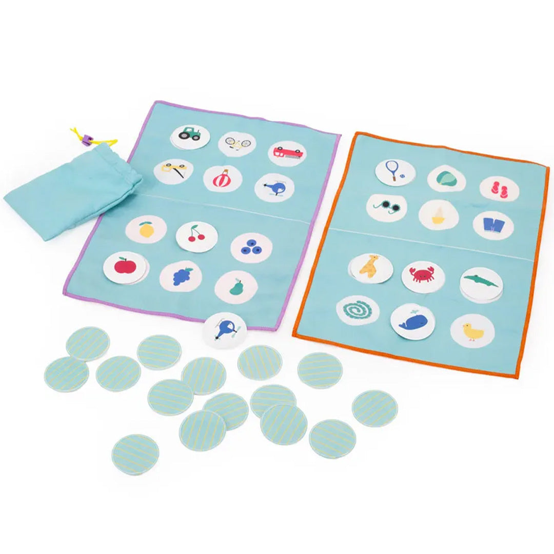 Quut reisspel bingo met twee blauwe stoffen speelborden, fiches met figuren en een zakje op een witte achtergrond.