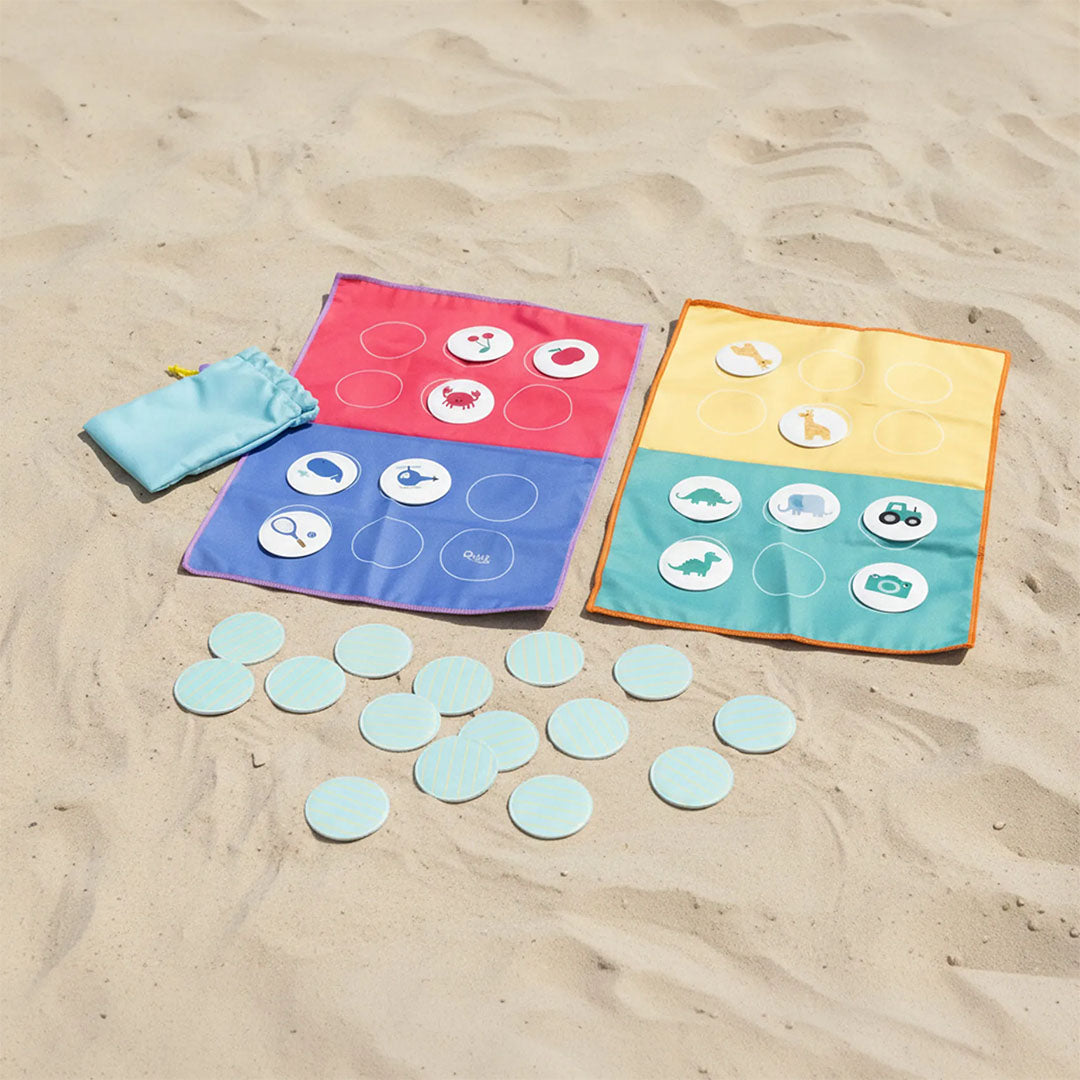 Quut reisspel bingo met twee kleurrijke stoffen speelborden, fiches met figuren en een zakje op het zand.