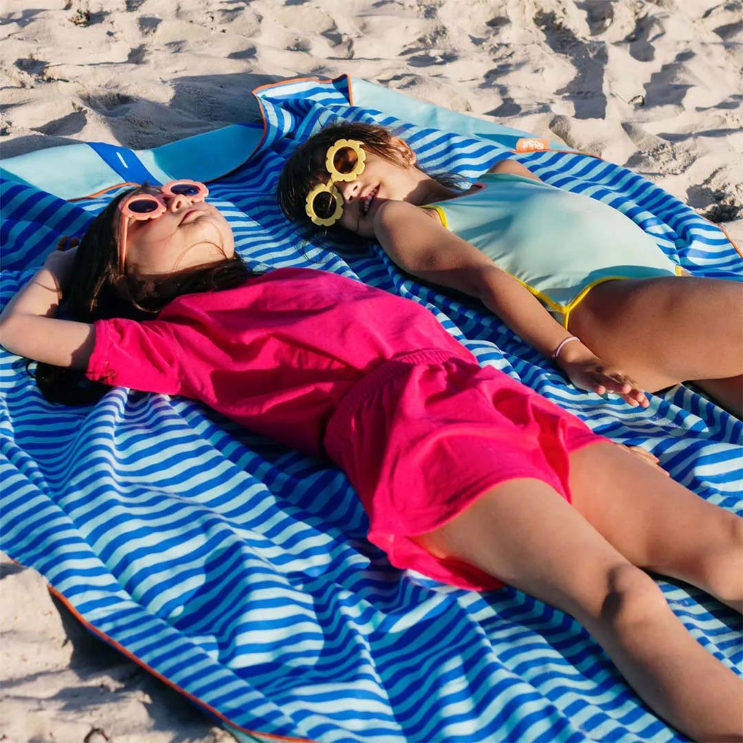 Twee meisjes liggen te zonnen op de gestreepte kant van de quut speelhanddoek op het strand.