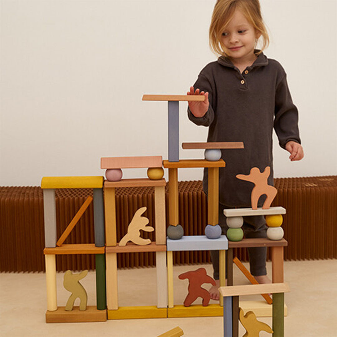 Een kind speelt met Raduga Grëz houten bouwblokken en houten figuurtjes die een constructie vormen.
