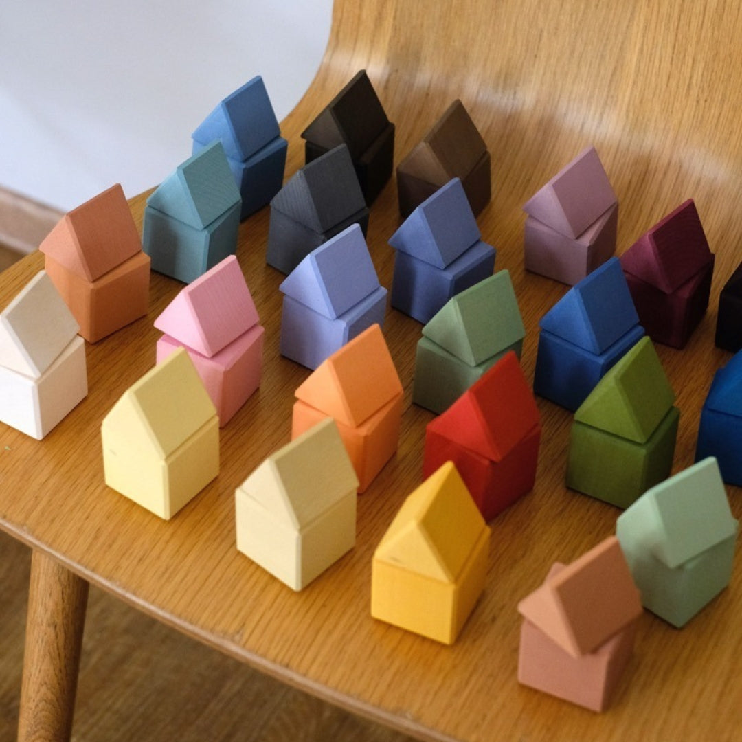 Veel kleine, veelkleurige houten huisvormige bouwblokken liggen verspreid op een houten stoel.