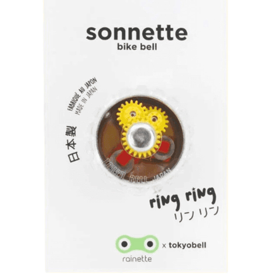 Verpakking van de rainette fietsbel met zicht op het mechanisme met gele tandwielen.