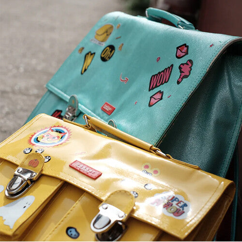 Twee schooltassen, een gele en een turquoise, beide versierd met rainette reflecterende stickers.