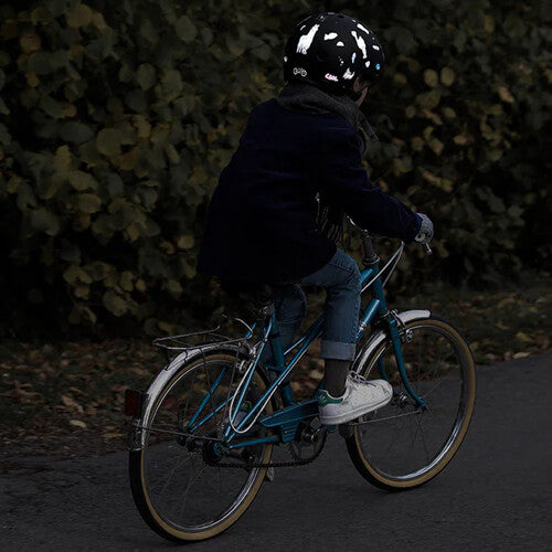 Kind fietst in het donker met een helm versierd met rainette reflecterende stickers.
