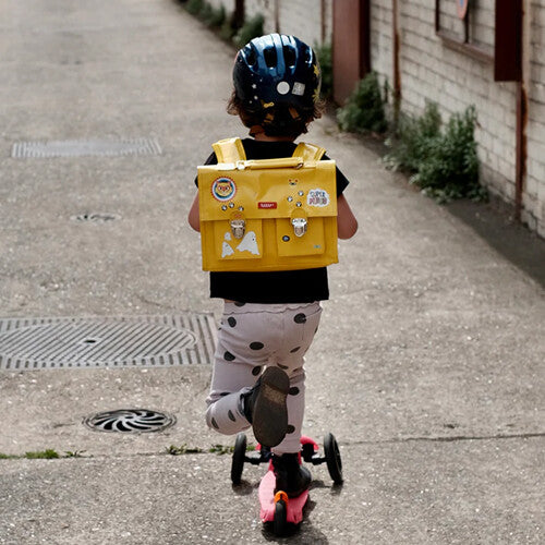 Kind met een gele schooltas en een helm met rainette reflecterende stickers rijdt op een scooter.