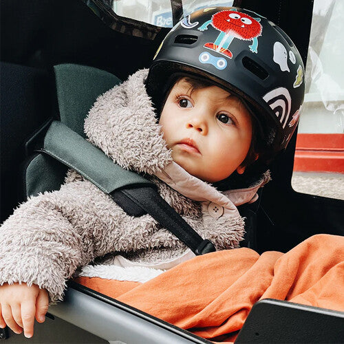 Peuter in een kinderwagen met een helm versierd met rainette reflecterende stickers.