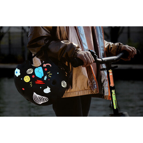 Persoon die een zwarte helm vasthoudt, versierd met diverse reflecterende rainette stickers.