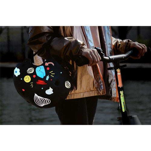 Een zwarte helm met oplichtende rainette reflecterende stickers hangt aan een scooter.