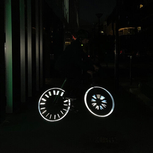 Een fietser in het donker met Rainette spaakreflectoren die fel oplichten op de wielen.