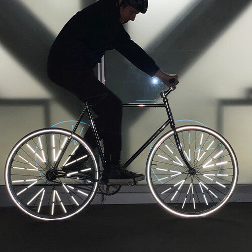 Een fietser in het donker met Rainette spaakreflectoren die fel oplichten op de wielen.