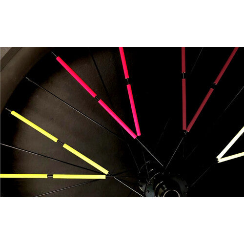 Detail van een fietswiel in het donker met oplichtende roze, gele en witte rainette spaakreflectoren.
