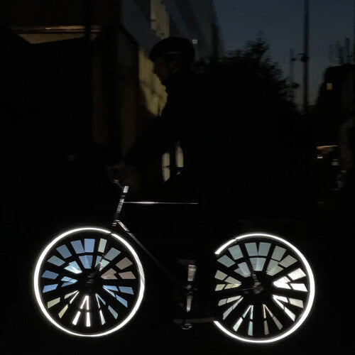 Een fietser in het donker met rainette spaakreflectoren die een oplichtend patroon vormen op de wielen.