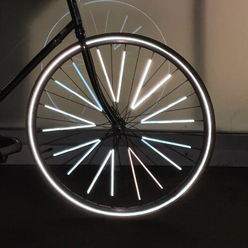 Een fietswiel in het donker met fel oplichtende rainette spaakreflectoren op de spaken.