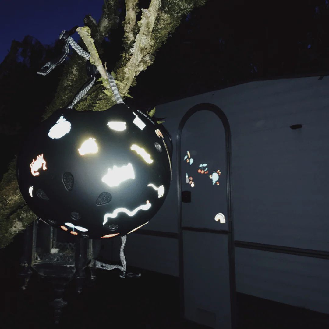 Een zwarte helm met reflecterende Rainette stickers die oplichten in het donker, hangend aan een boomtak.