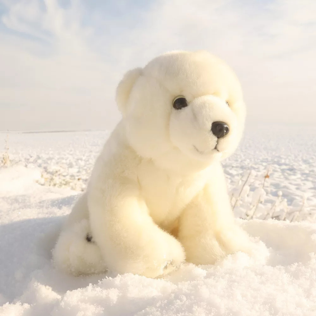 Pluchen knuffelijsbeer zittend in een besneeuwd landschap.