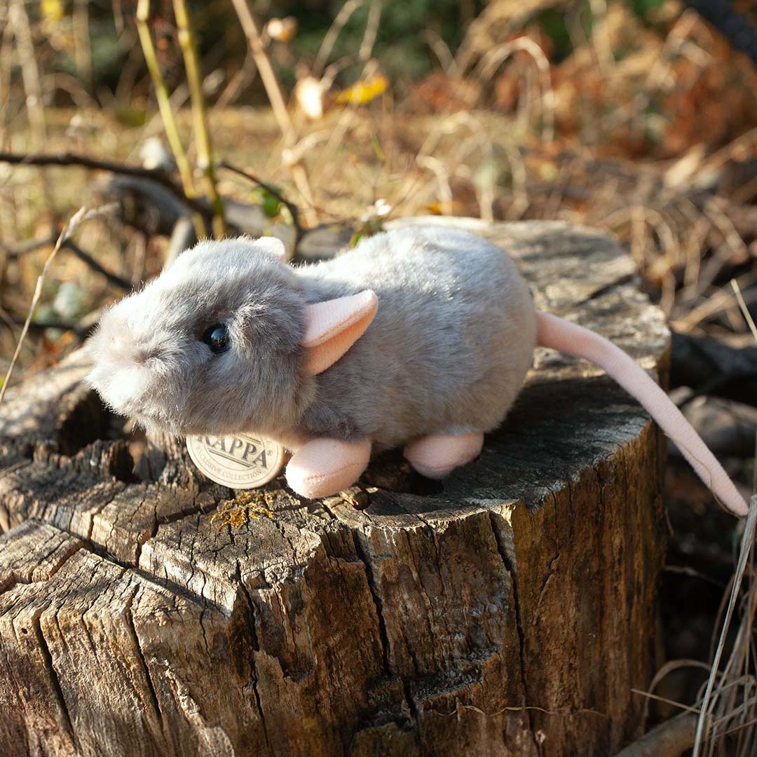 Rappa knuffelmuis van grijs pluche op een boomstronk in de natuur.