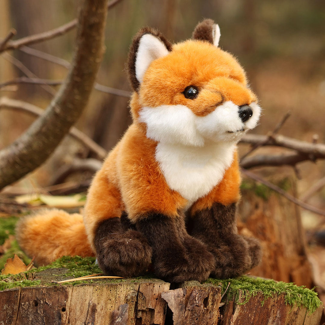 Knuffelvos zittend op een boomstronk in een bosrijke omgeving.