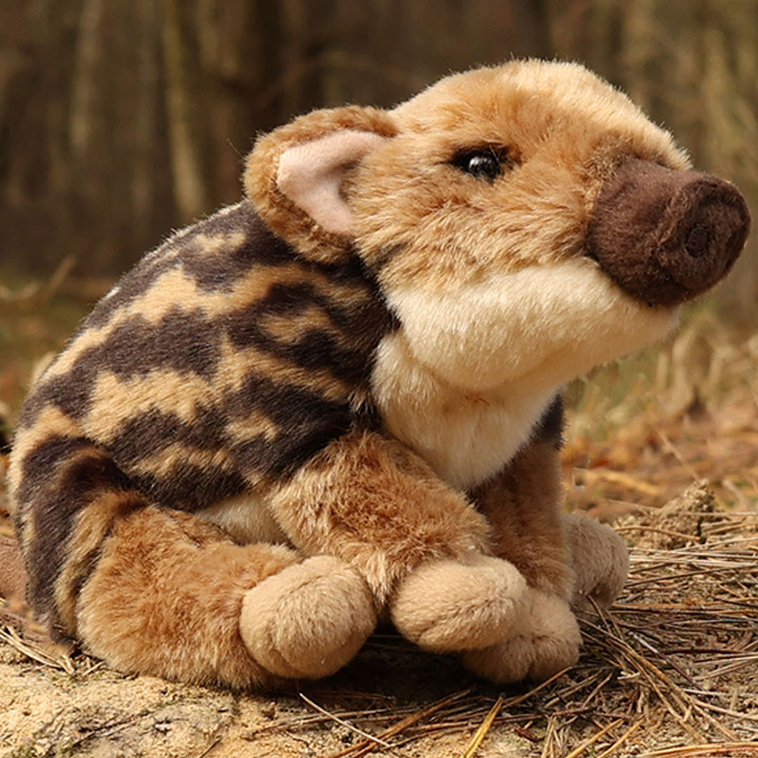 Rappa pluchen baby wild zwijn knuffel zittend in een bosrijke omgeving.