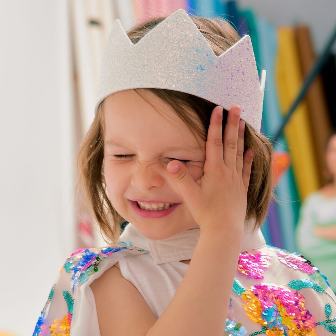 Een kind draagt de Ratatam witte glitter kroon en een kleurrijke cape.