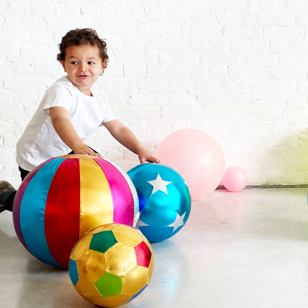Een kind speelt op de grond met een ratatam veelkleurige gestreepte circus speelbal en andere ballen.