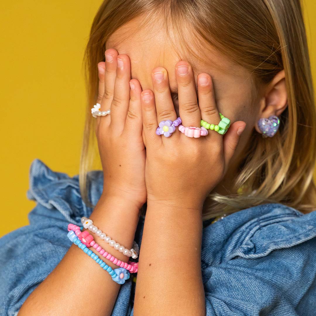 Een kind met kleurrijke kralenarmbanden en ringen met bloemenmotief.