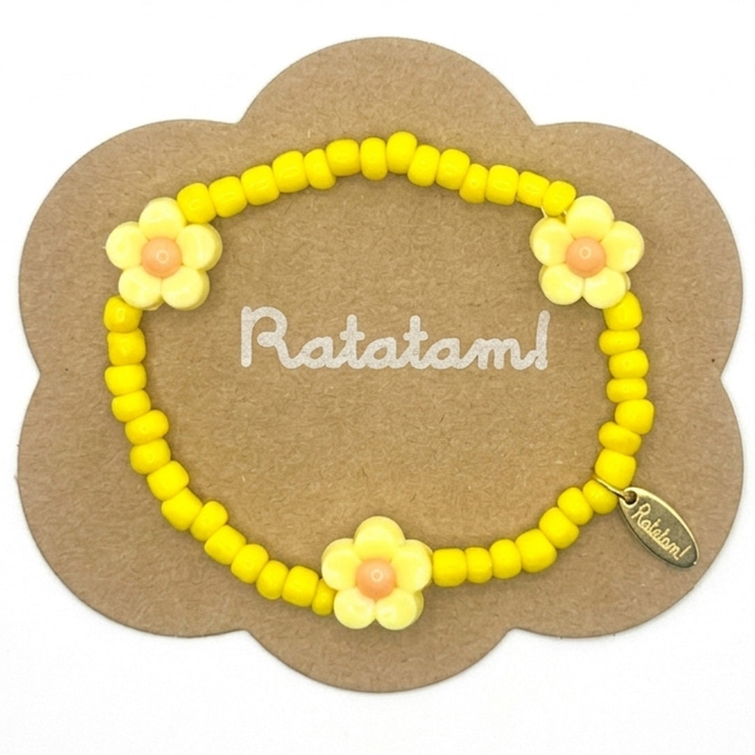 Verpakking van de Ratatam kinderarmband met gele kralen en bloemkralen op een bruin kartonnen kaart.