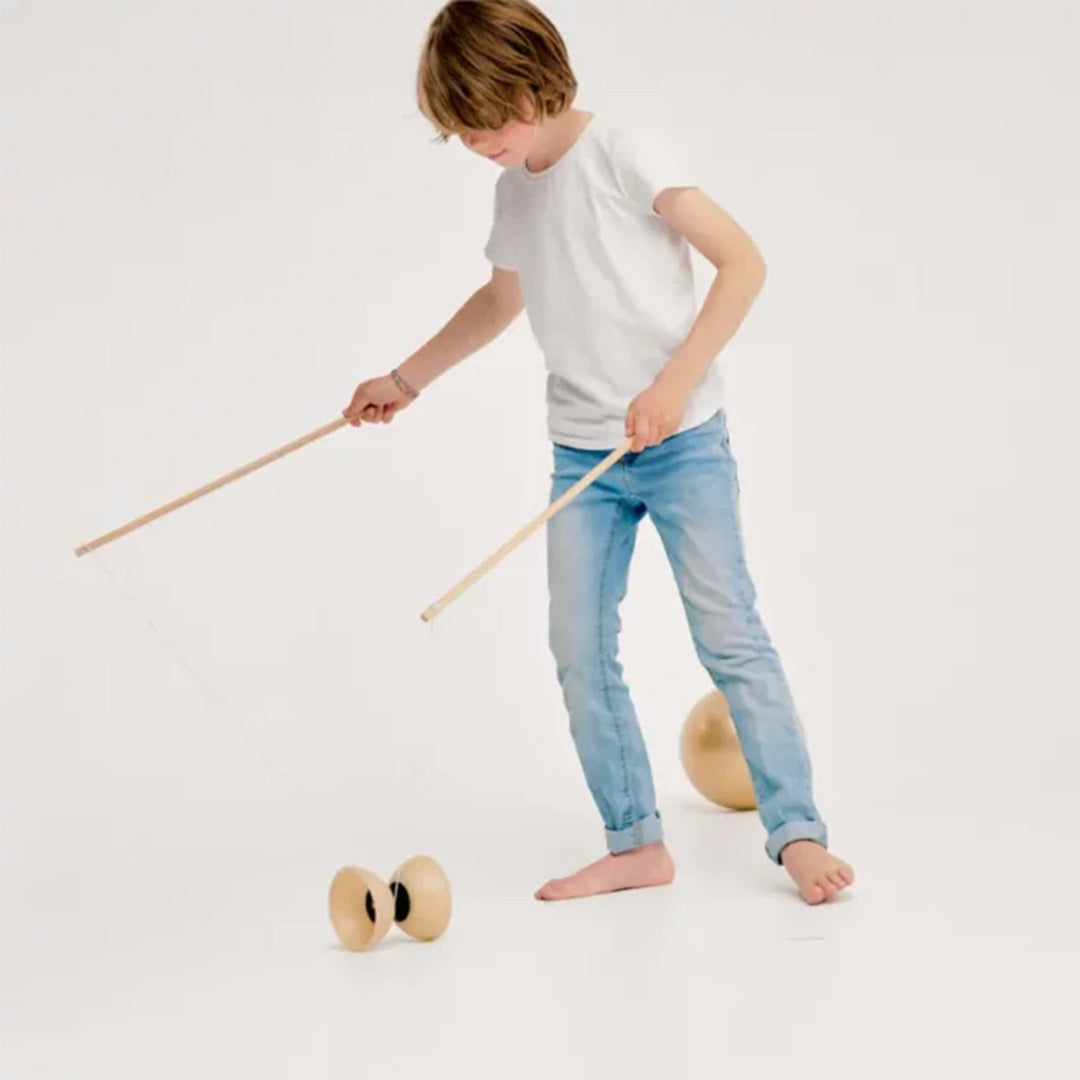 Een kind speelt met een houten diabolo en twee houten stokken op een witte achtergrond.