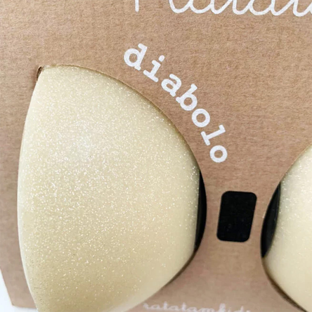 Detail van de beige, glimmende diabolo door de kartonnen verpakking met het woord 'diabolo'.