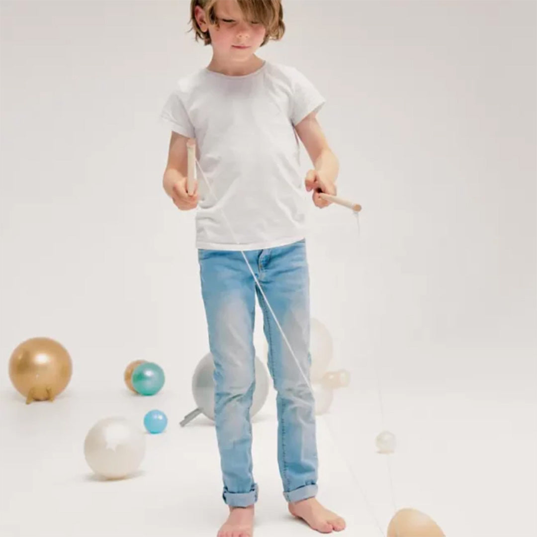 Een kind staat met de houten stokken en het touw van een diabolo, omringd door ballonnen.
