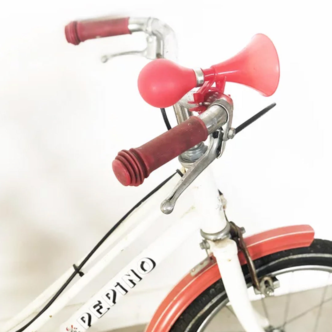 Ratatam rode fietstoeter gemonteerd op het stuur van een witte kinderfiets.