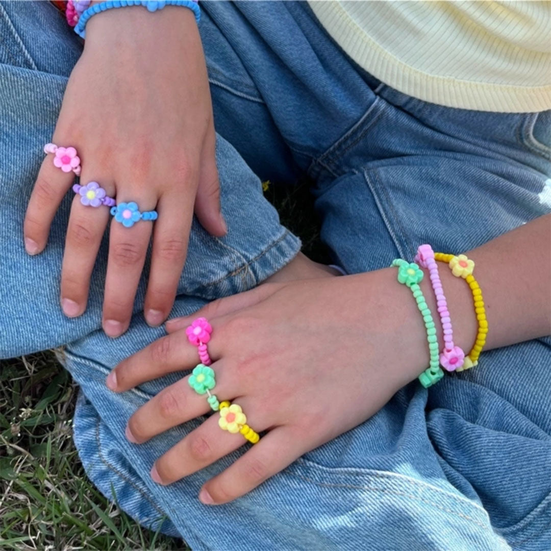Close-up van kinderhanden met diverse kleurrijke kralenringen en armbanden met bloemen.