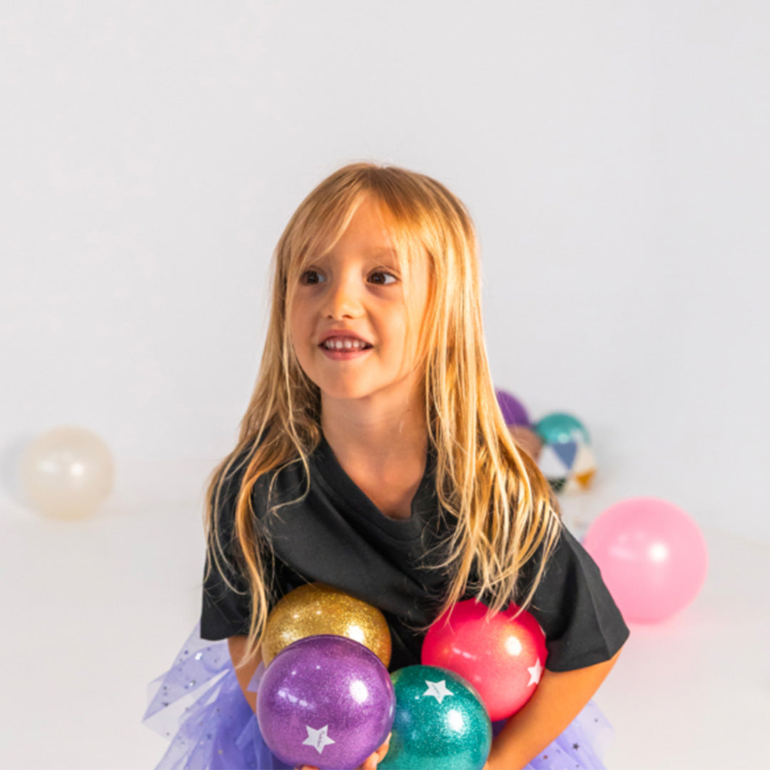 Meisje met lang blond haar houdt meerdere Ratatam glitter speelballen in verschillende kleuren vast.