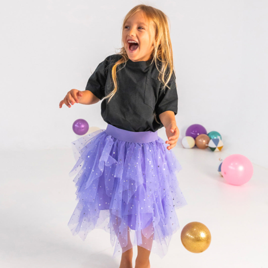 Een lachend meisje in een paarse tutu springt terwijl een gouden glitter speelbal in de lucht is.