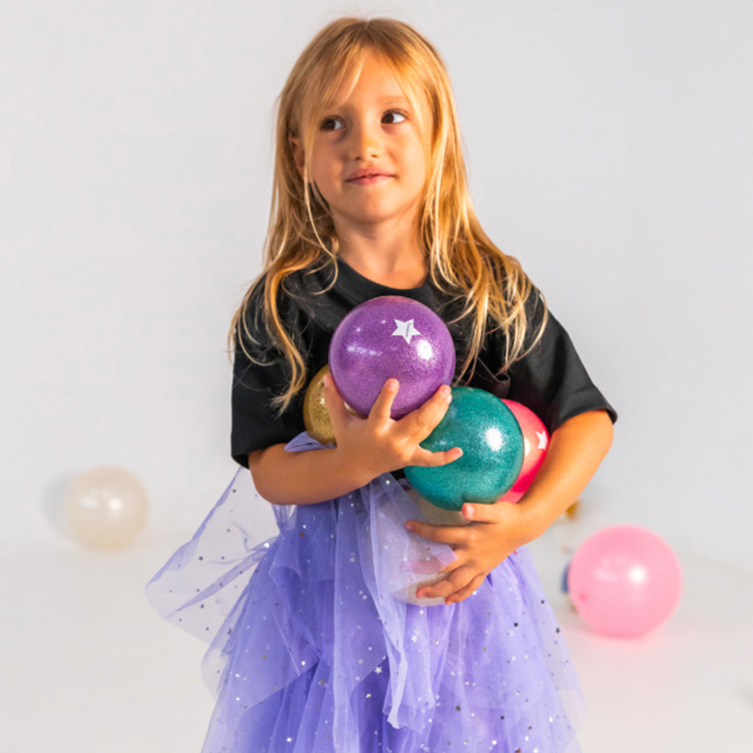 Een meisje met lang blond haar houdt meerdere Ratatam glitter speelballen in verschillende kleuren vast.