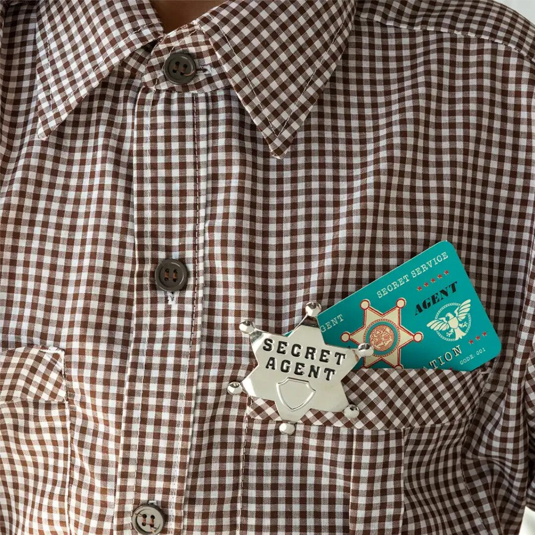 De secret agent badge en ID-kaart van Rex London in de borstzak van een bruin geruit overhemd.