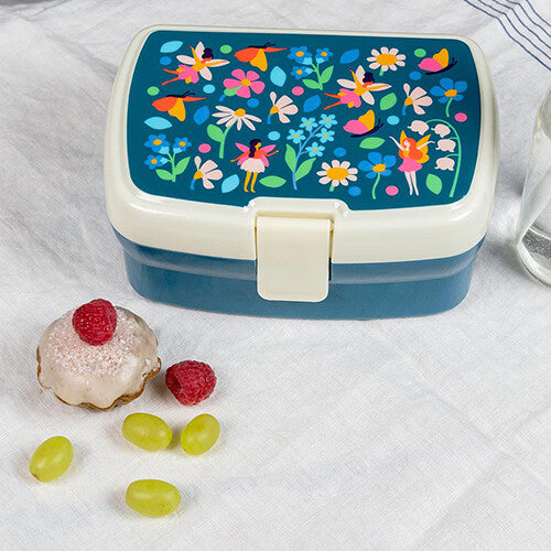 Rex London plastic broodtrommel met feeën- en bloemenpatroon op een witte doek met fruit en een cupcake ernaast.