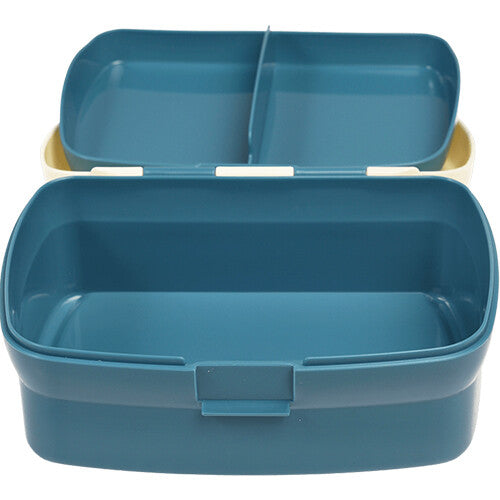 Open Rex London plastic broodtrommel met blauwe onderkant en crèmekleurige deksel, met het vakjesblad in de deksel.