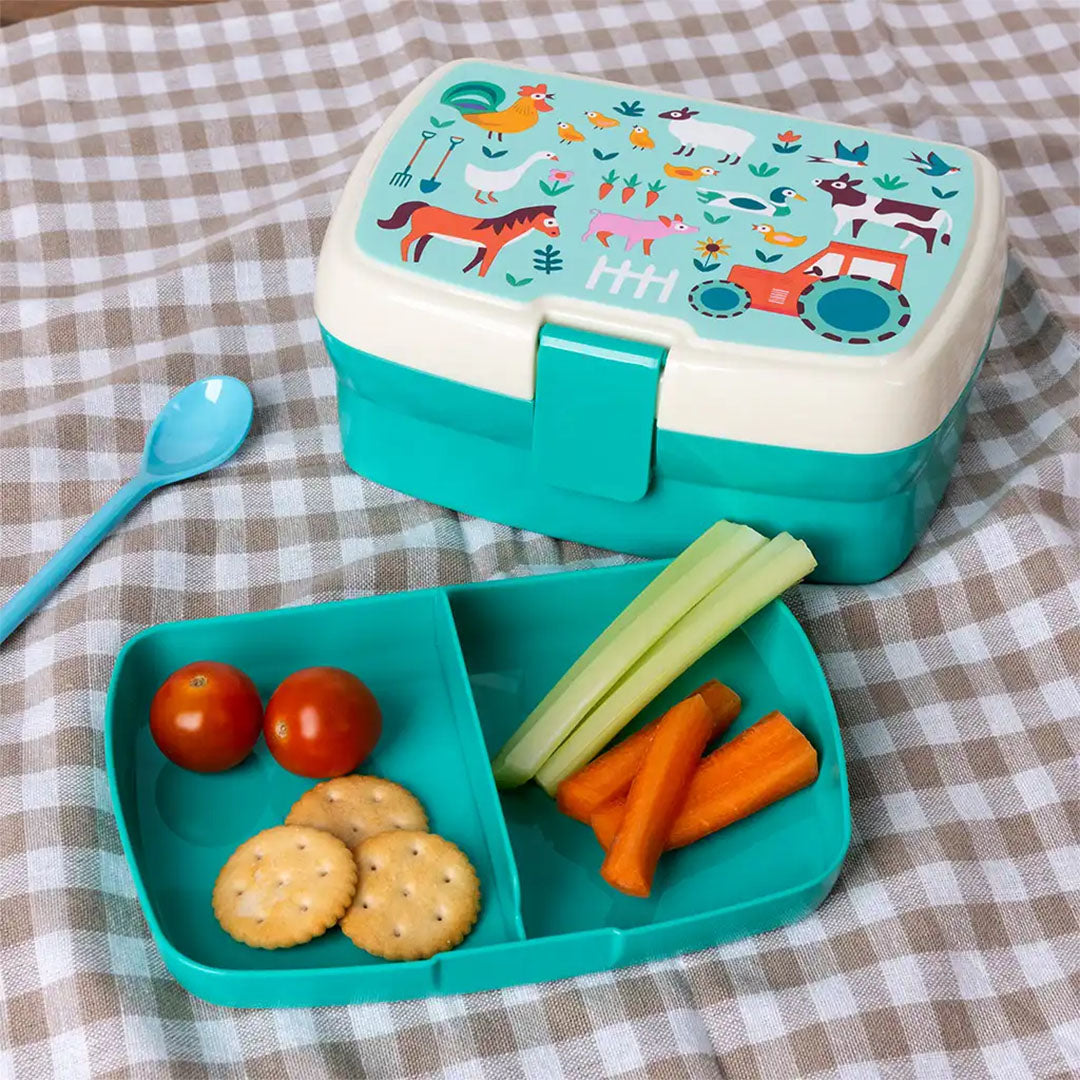 Open Rex London kinderbroodtrommel met vakjesblad gevuld met groenten en crackers, op een geruite ondergrond.