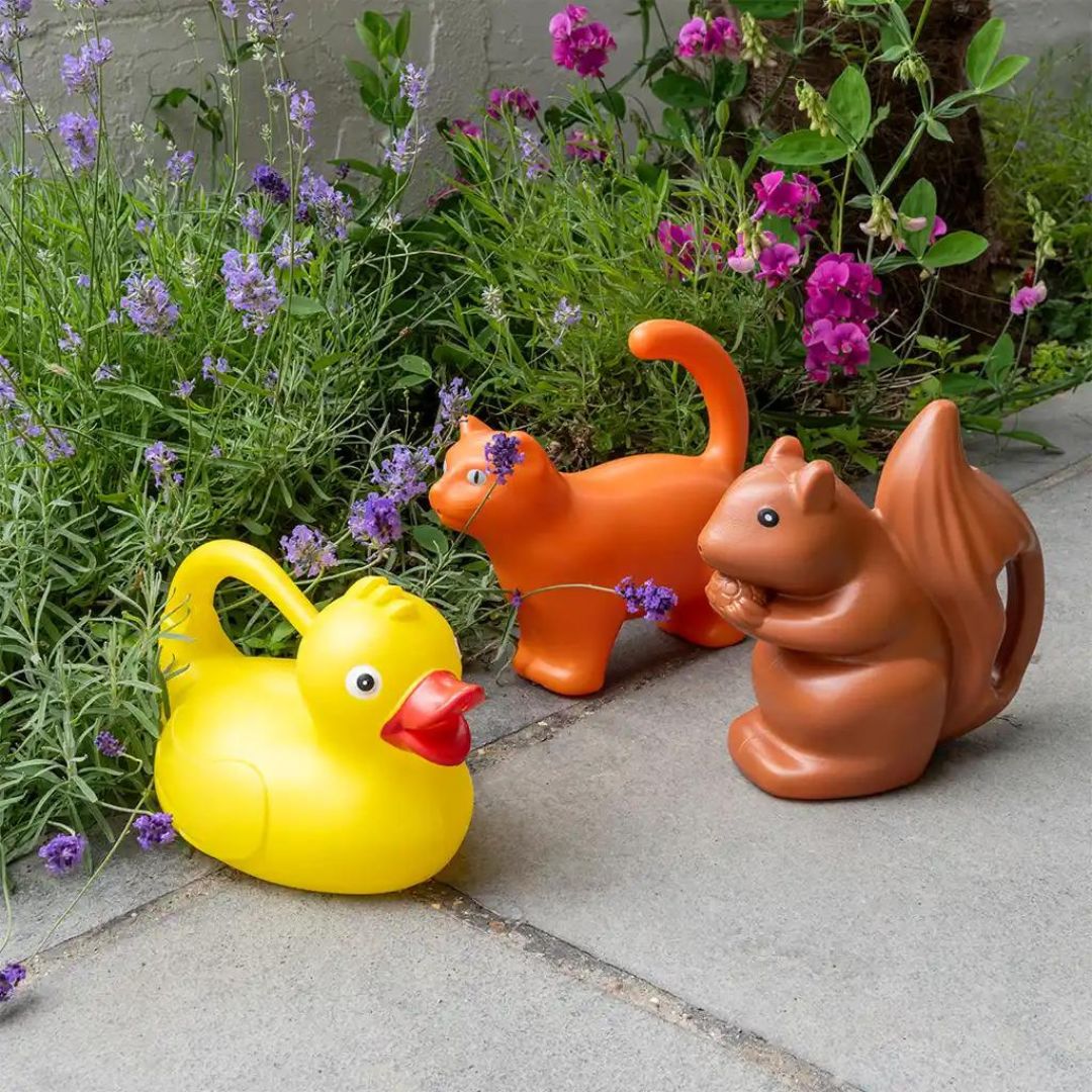 Drie plastic gieters in de vorm van een eekhoorn, eend en kat staan op een terras.