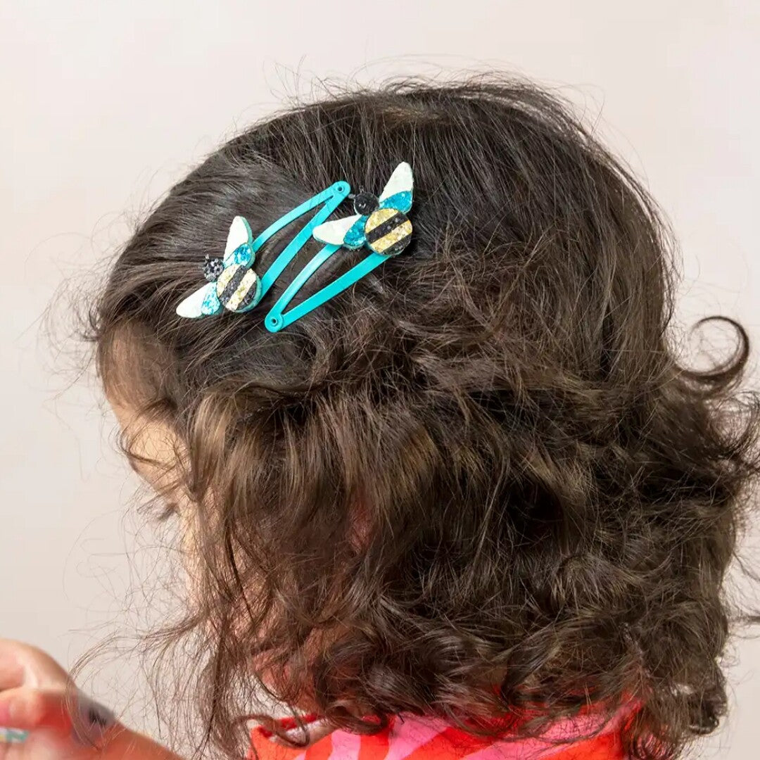 Een kind draagt twee haarspeldjes met glitterbijen in haar bruine krullende haar.