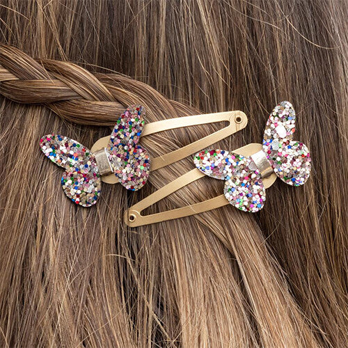 Twee Rex London haarspeldjes met glittervlinders in bruin haar.