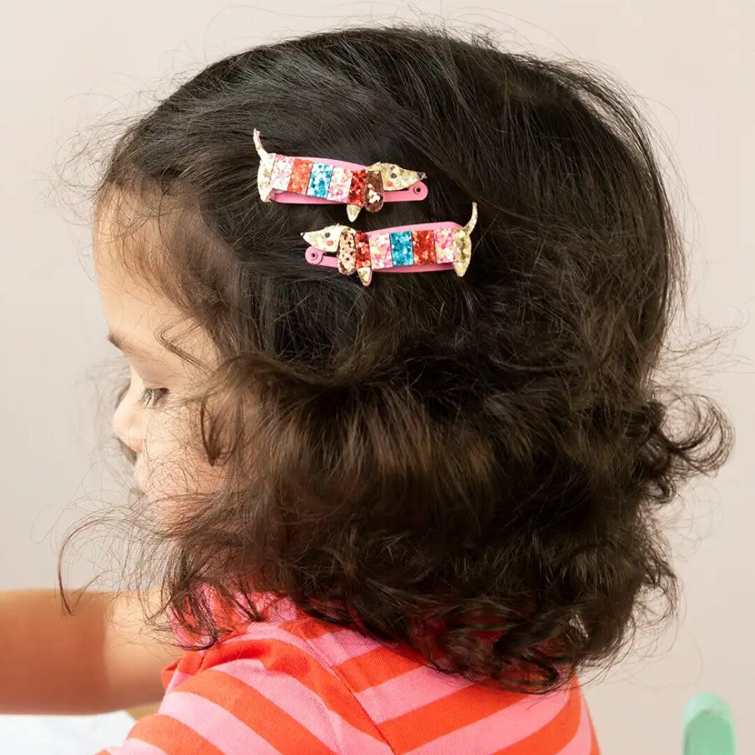 Een kind draagt twee worsthond haarspeldjes met glitter in haar donkere krullende haar.